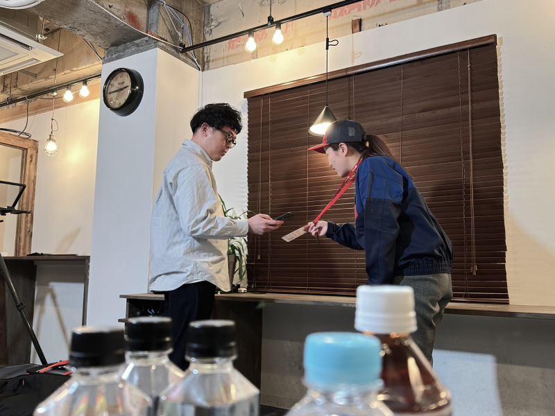 スタッフ役の社員がお客様役の社員へ首から下げた案内用POPを見せてご案内している様子